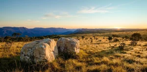 Dois grandes blocos de pedra clara lado a lado sobre capim dourado no alto de uma chapada do cerrado, com serras azuladas e o sol nascendo no horizonte